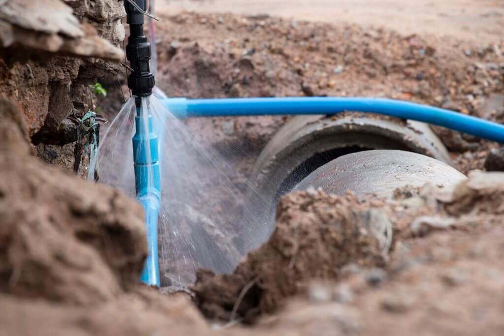 Blue pipe with water spraying out of it into mud. Total Water Solutions Home page
