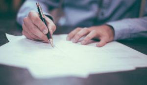 Man writing and signing a pile of papers