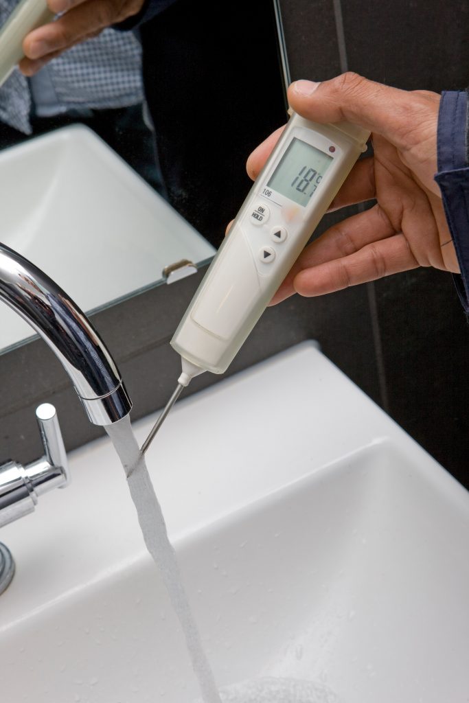 Total Water Solutions. Man testing the temperature of water coming out of a tap.