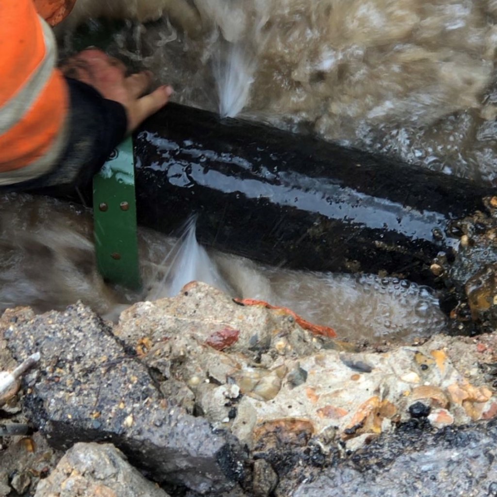Someone in high vis jacket adjusting a leaking pipe in the ground